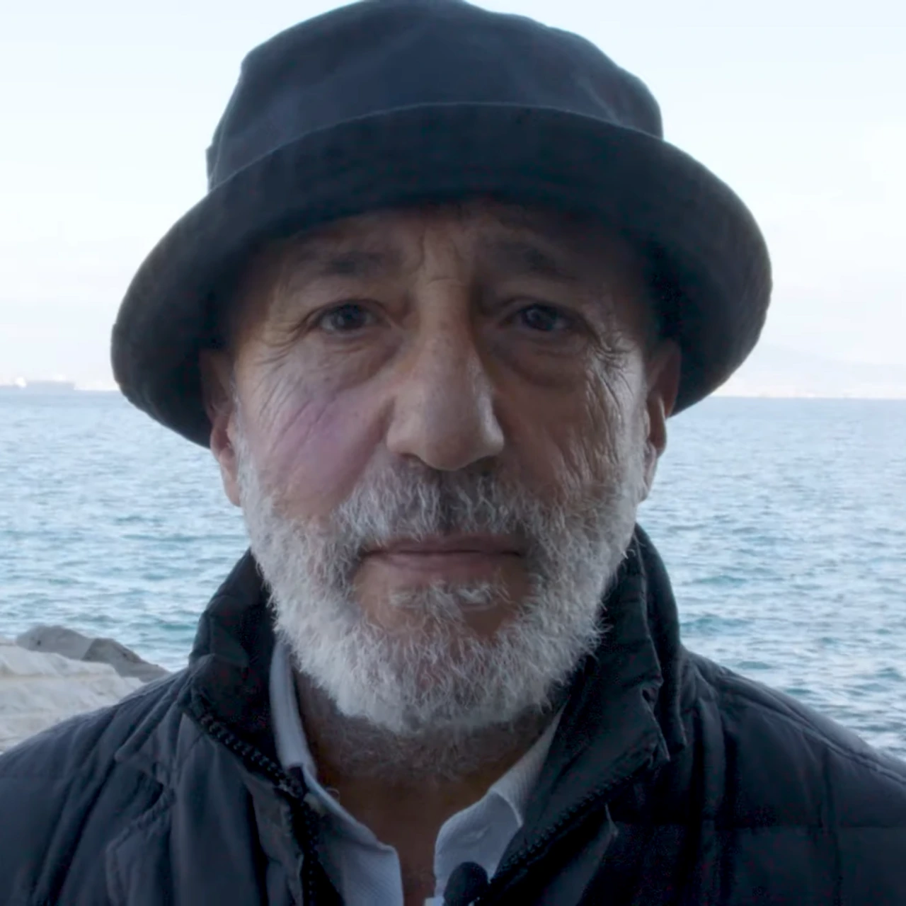 Portrait of DJ Orazio RispO by the sea, wearing a dark hat and jacket
