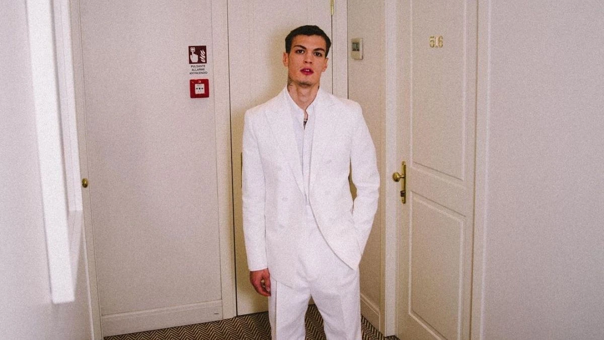 Blanco standing in a white suit in a hallway, a clear editorial-style photo of the Italian singer Riccardo Fabbriconi.