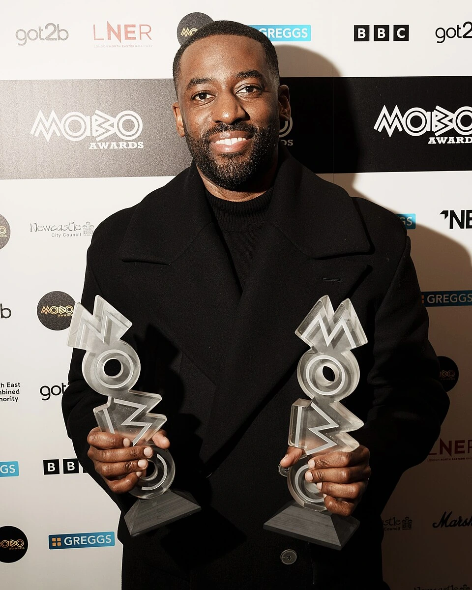 Ashley Thomas (Bashy) holding MOBO Awards trophies at a red carpet event