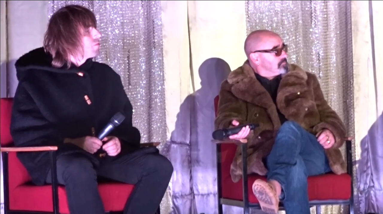 Paul Arthurs (Bonehead) seated at an event, holding a microphone.