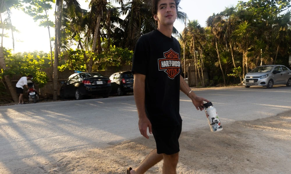 Ben Bader standing outdoors on a road with palm trees in the background, holding a water bottle.