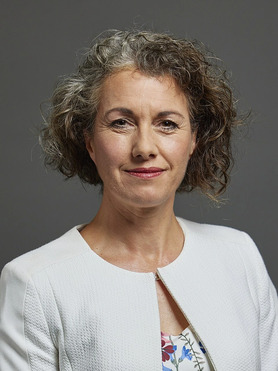 Portrait of Sarah Champion in a white jacket against a gray background.