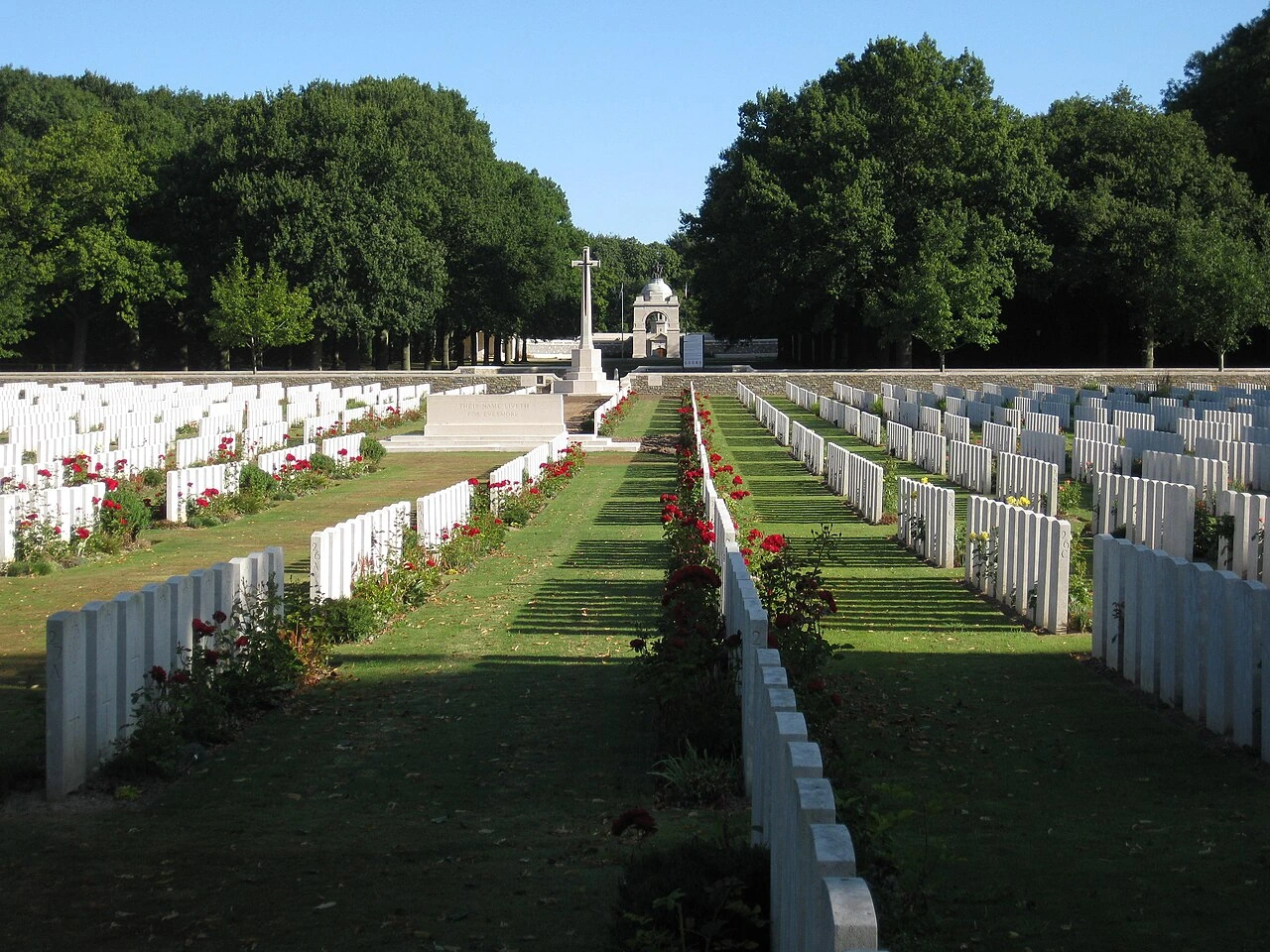 Cimetière militaire avec allées de pelouse clairsemée sous l’ombre des arbres, en France