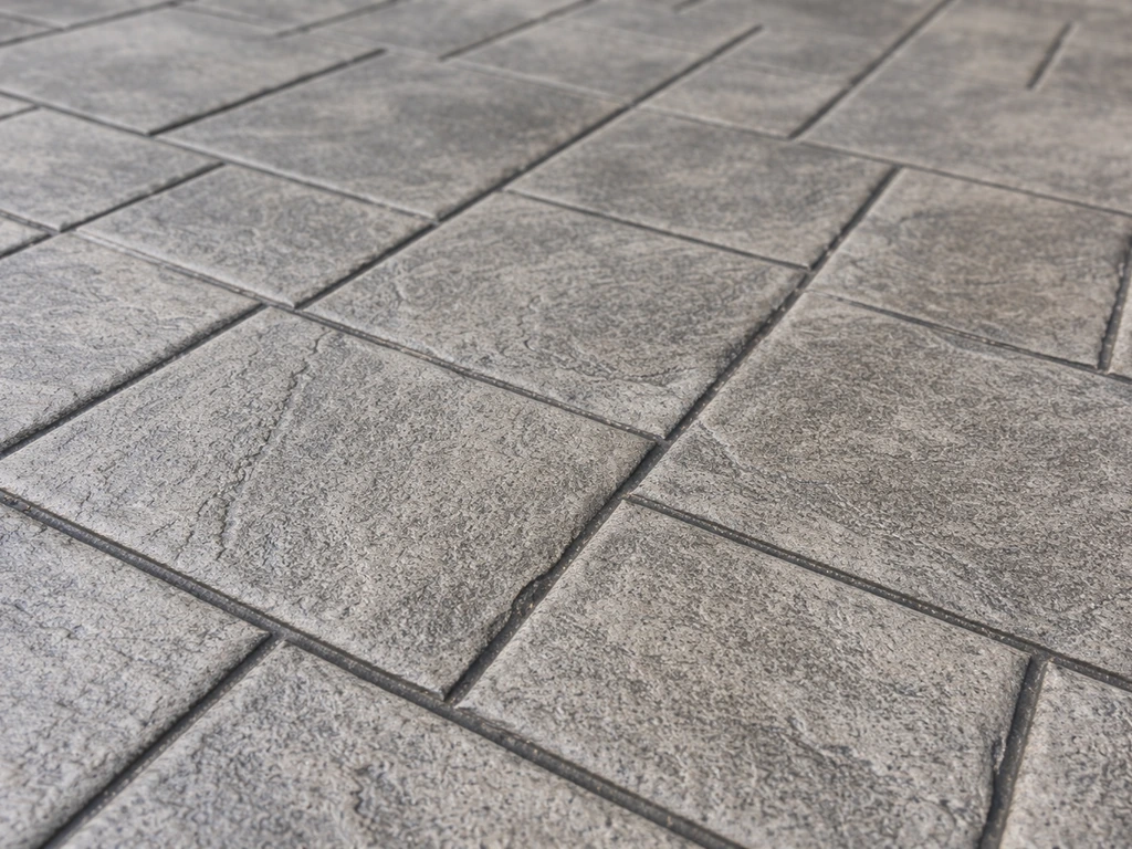 Closeup of stamped gray concrete patio showing a repeating pressed pattern.
