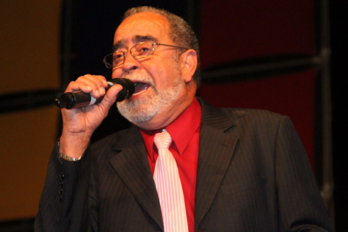 Andy Montañez singing into a microphone on stage in a suit and red shirt.