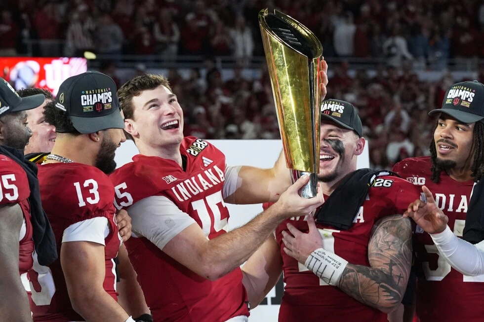 Fernando Mendoza celebrating with the team after a championship win, holding a trophy in an Indiana uniform