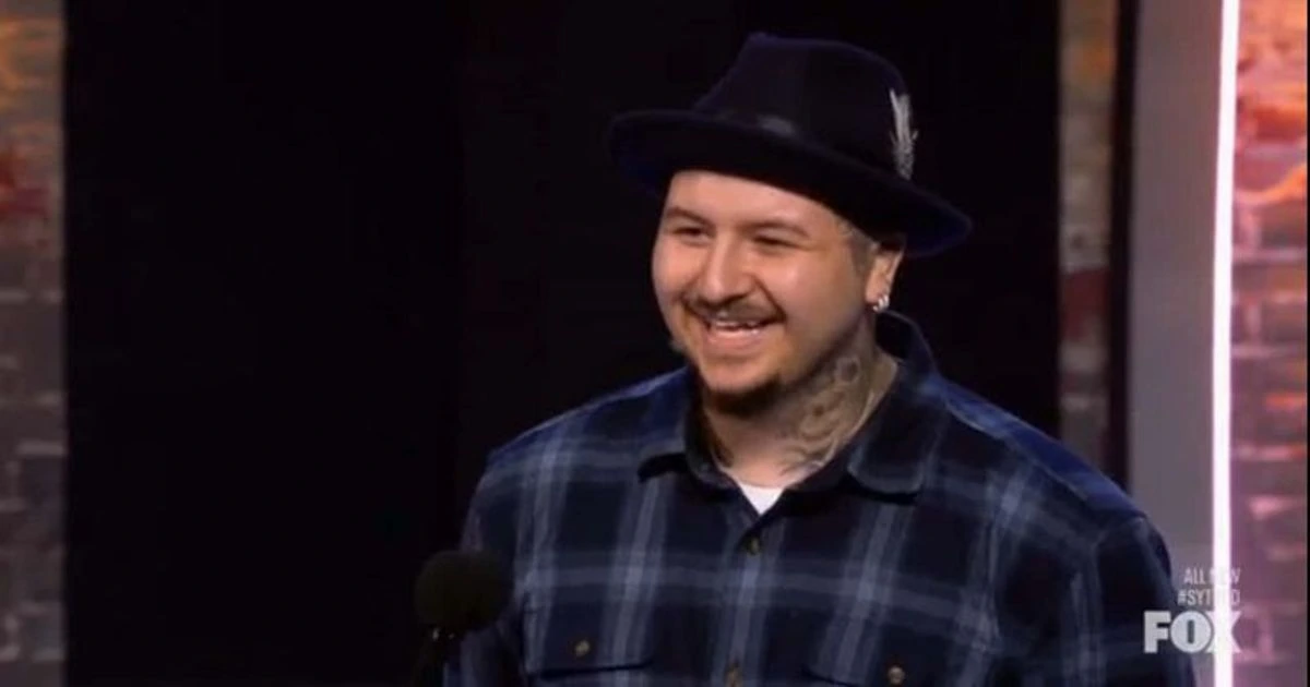 Armando Muñoz smiling on a television set wearing a hat and plaid shirt
