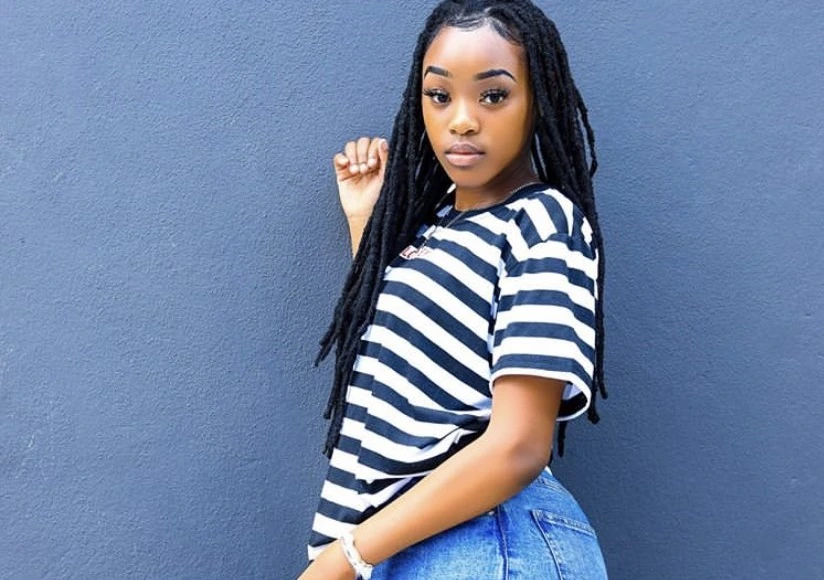 Andiswa Selepe posing against a blue wall in a striped shirt and jeans.