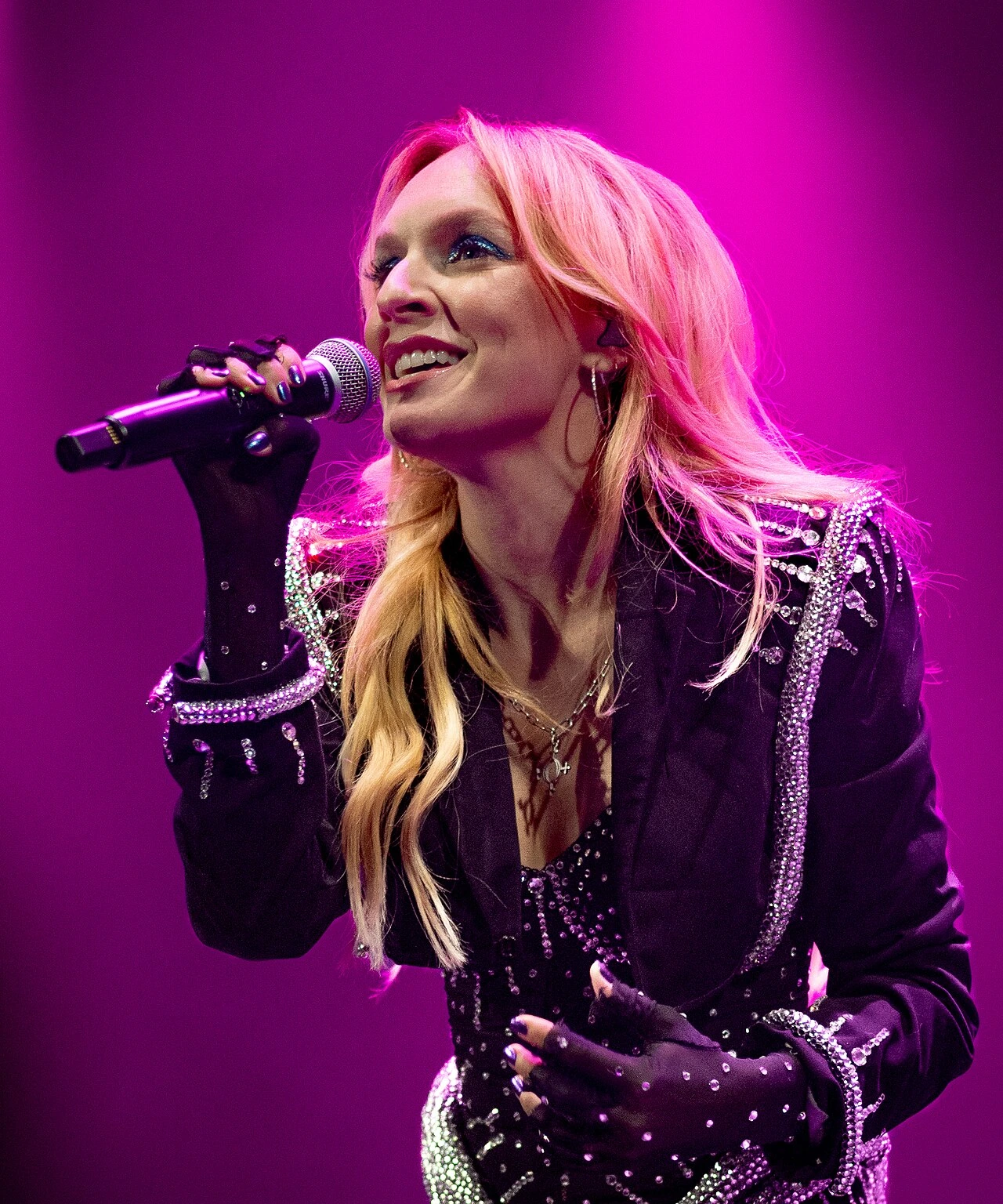 Zoë Montana Hoetzel (Zolita) performing on stage under pink lighting, holding a microphone and smiling.