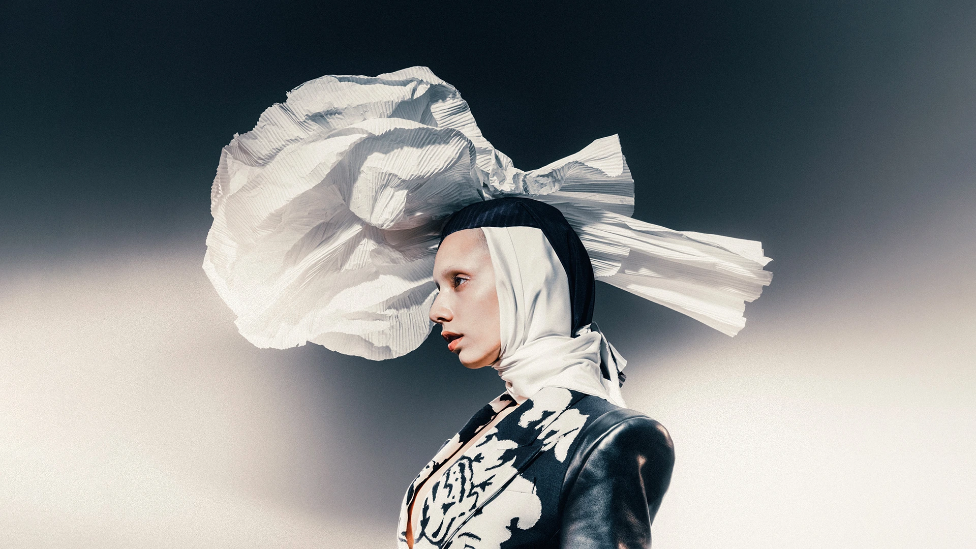 Jazzelle Zanaughtti in an editorial fashion portrait with a sculptural white headpiece and profile pose against a minima
