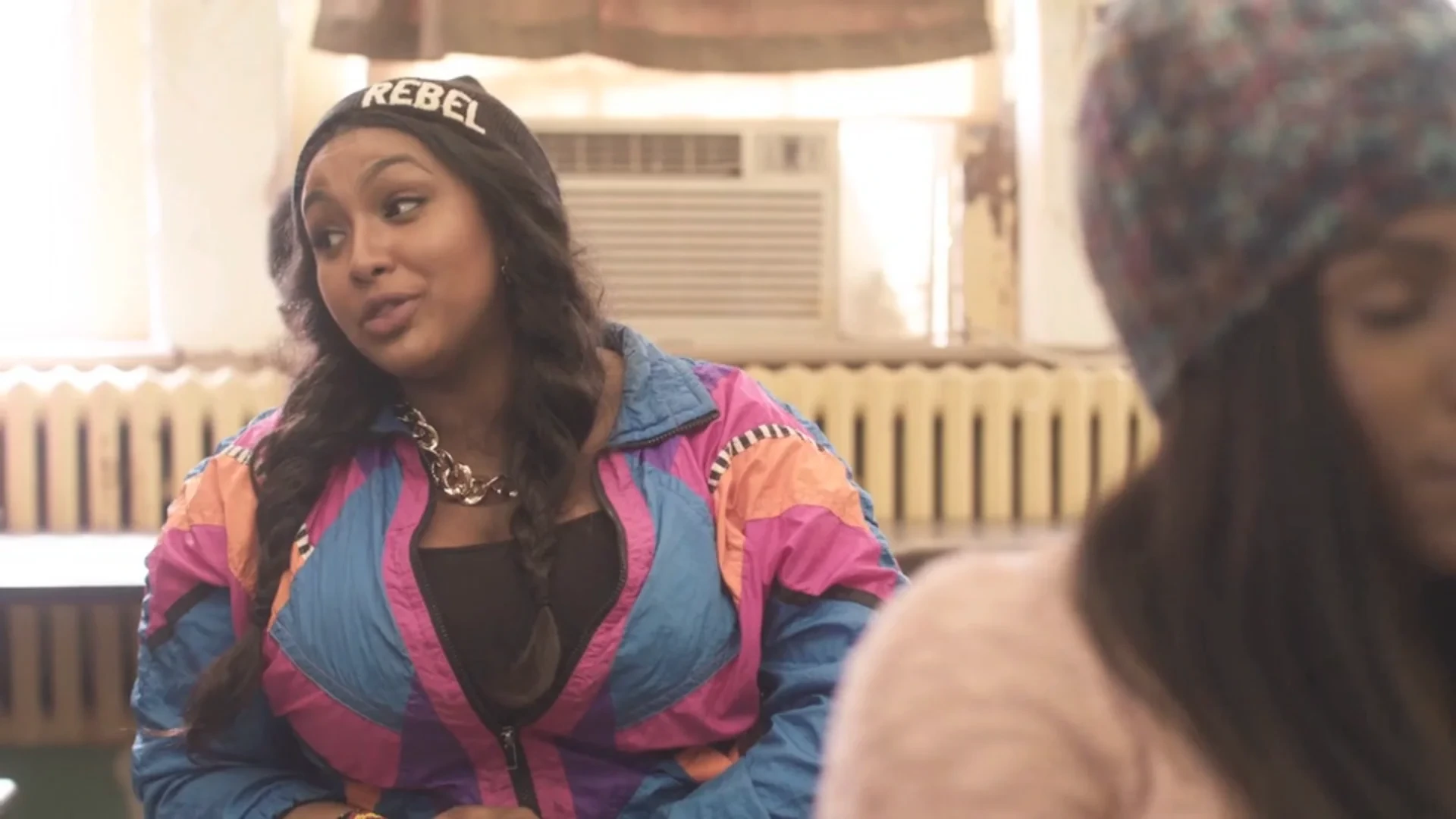 Nzinga Imani in a candid video still, wearing a colorful jacket and black cap