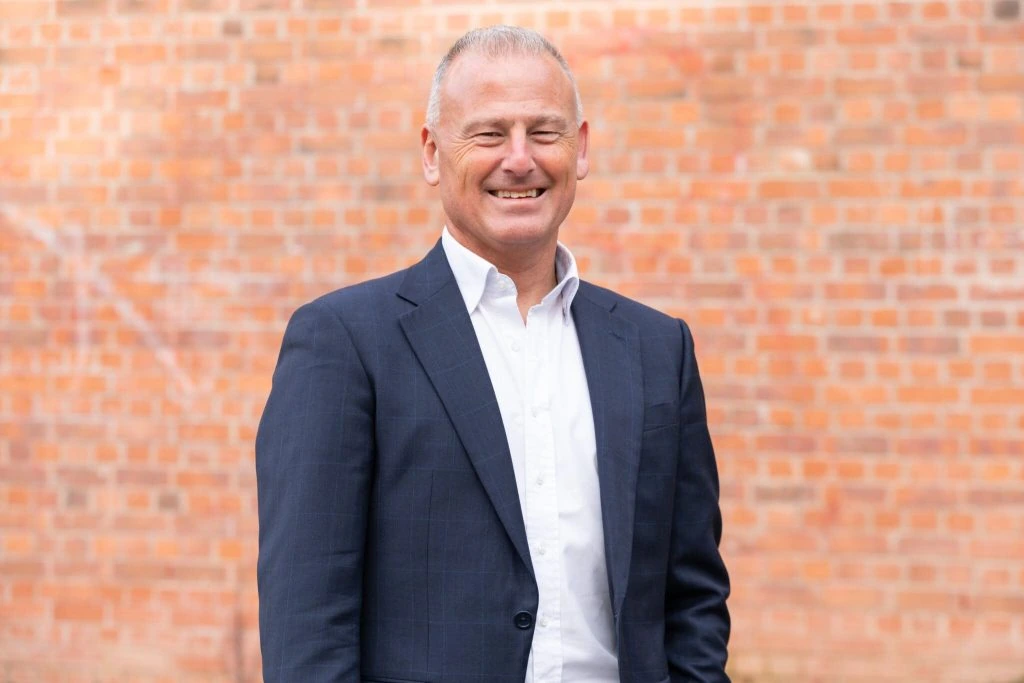 Winston Zahra smiling in a suit against a brick wall