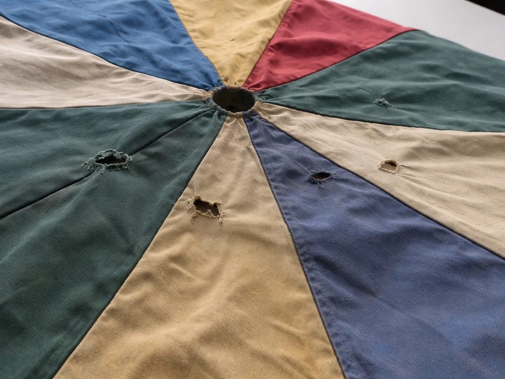 Umbrella canopy fabric spread flat with visible tears, holes, and faded panels near seams