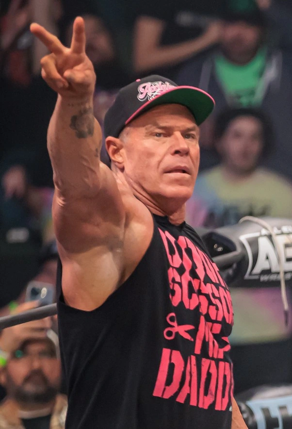 Billy Gunn in an AEW wrestling event, wearing a cap and sleeveless shirt, raising two fingers.