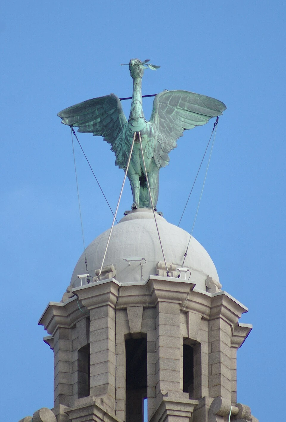 A photograph of a Liver bird statue atop a building against a blue sky.