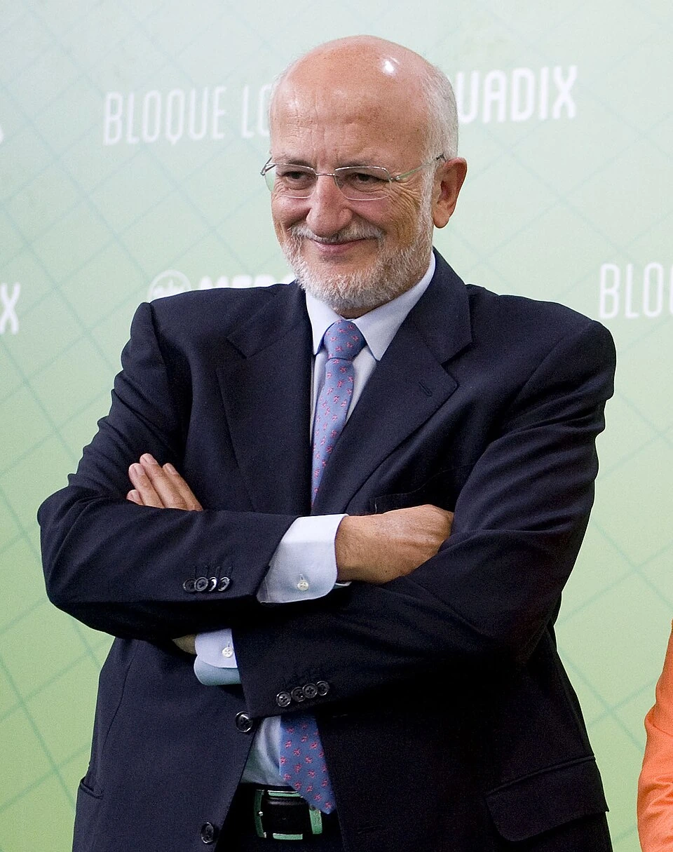 Juan Roig smiling in a suit and tie with arms crossed at an event backdrop.