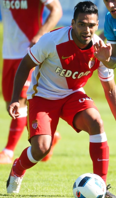 Radamel Falcao García Zárate in a red-and-white Monaco kit during a match, dribbling a soccer ball on the field.