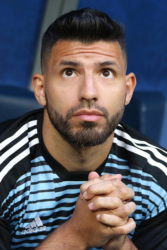 Sergio Agüero in a close-up portrait wearing an Argentina training top, looking upward with clasped hands.