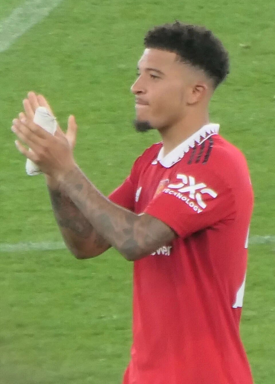 Jadon Sancho in a Manchester United match, clapping on the pitch in a red kit.