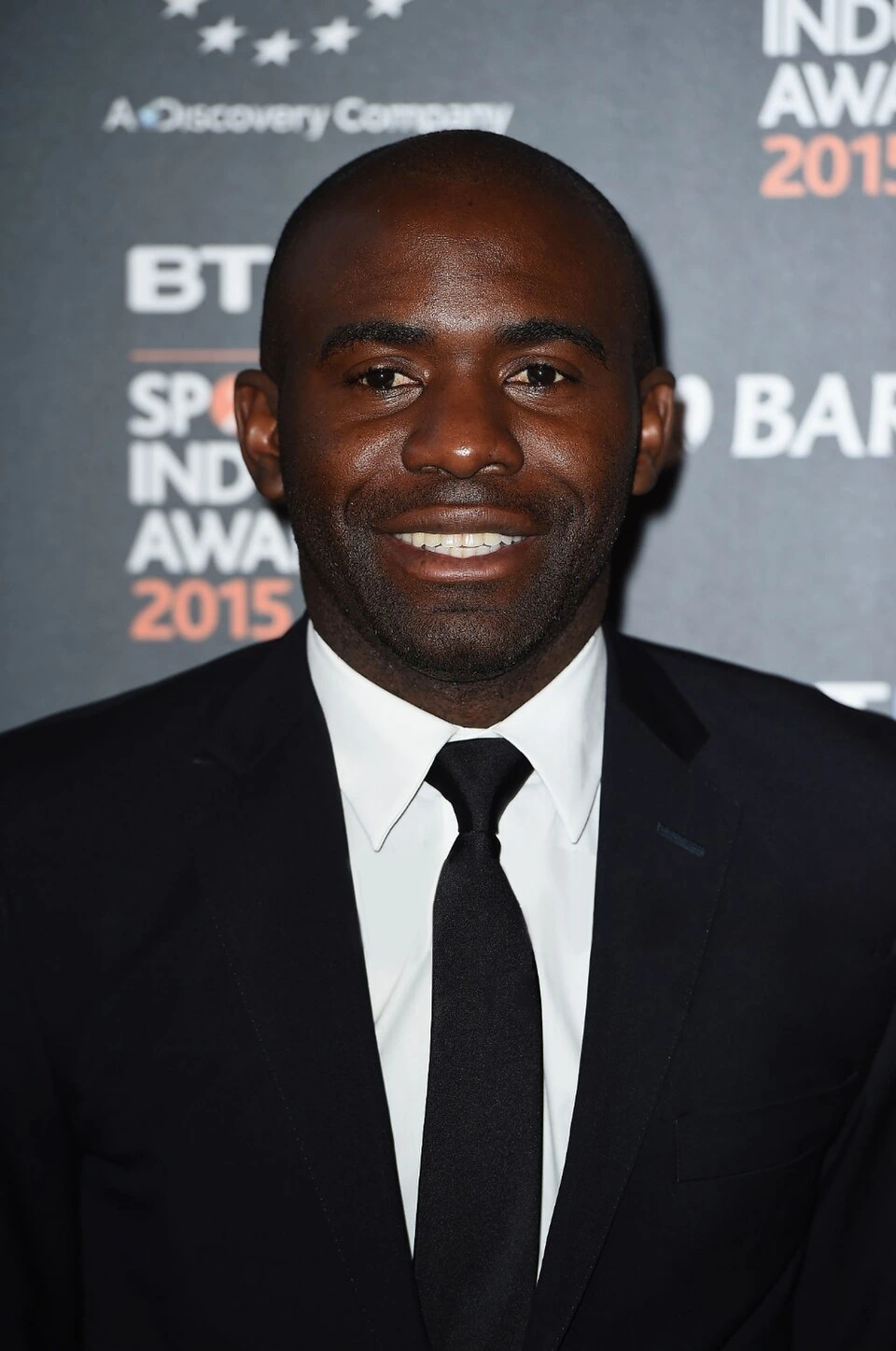 Fabrice Muamba at a formal event in a suit and tie, smiling in front of a backdrop