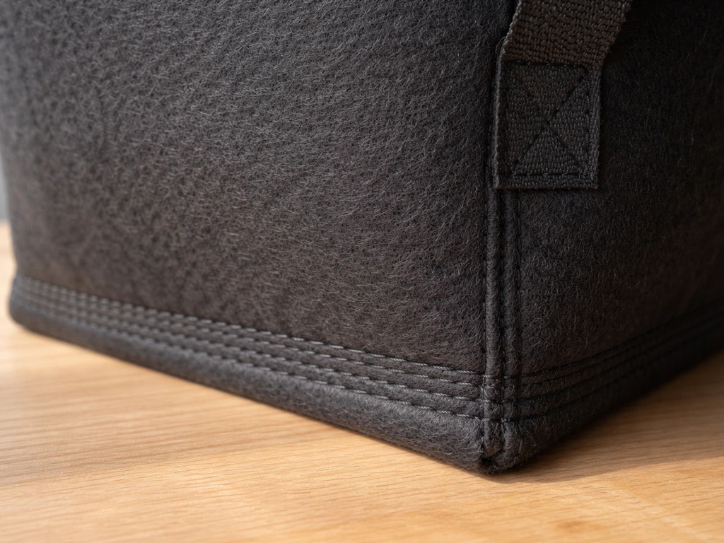 Close-up of a thick nonwoven grow bag fabric, showing reinforced double-stitch seams and a sturdy handle