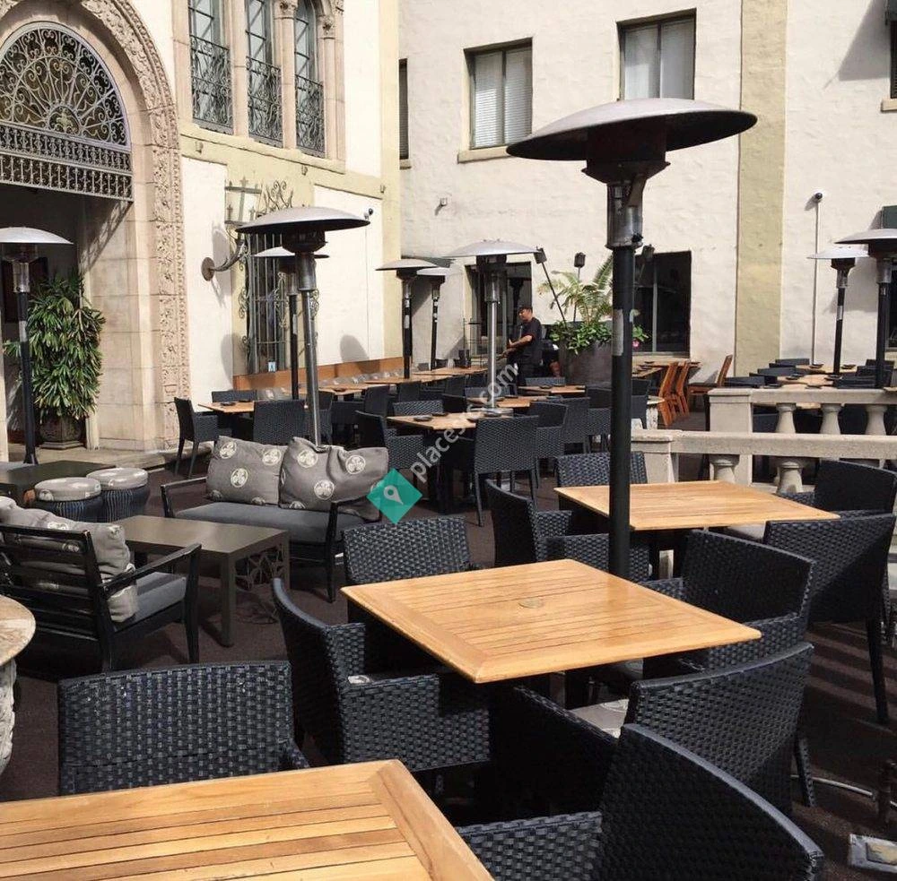 Outdoor patio dining area with tables, chairs, and heaters in a courtyard setting