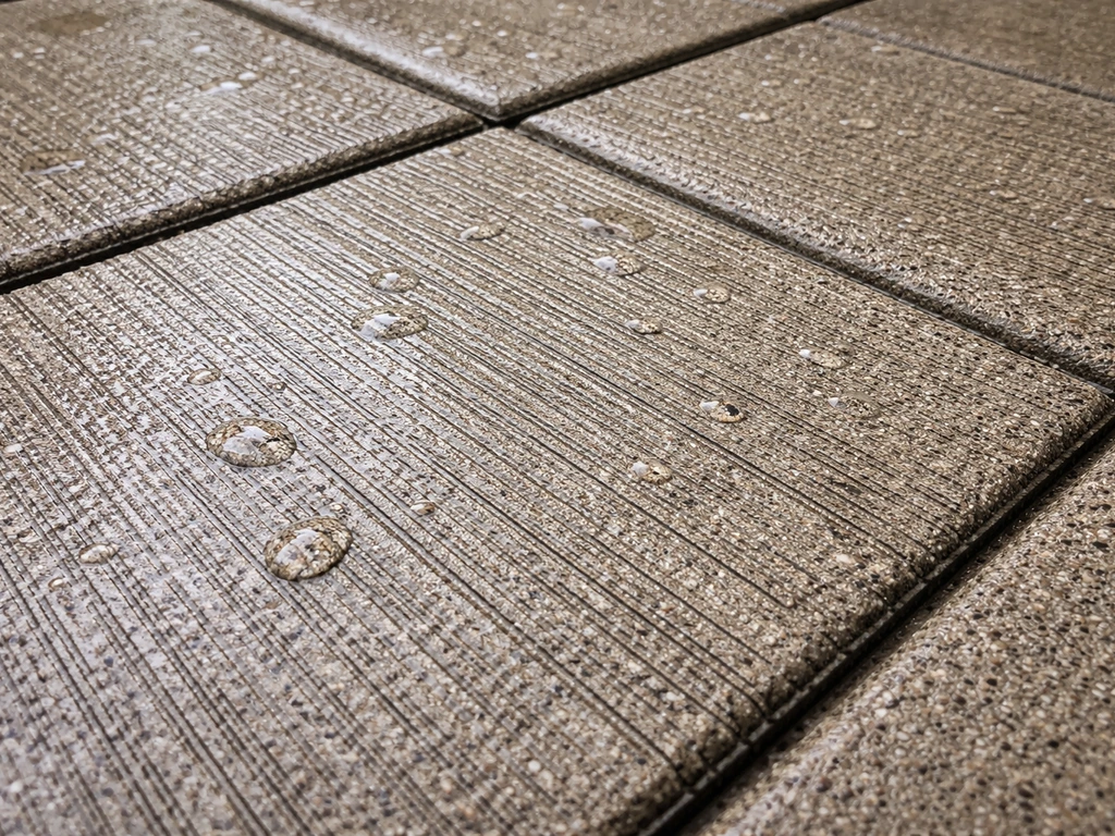 Close-up of wet textured concrete pavers showing traction grooves for slip resistance