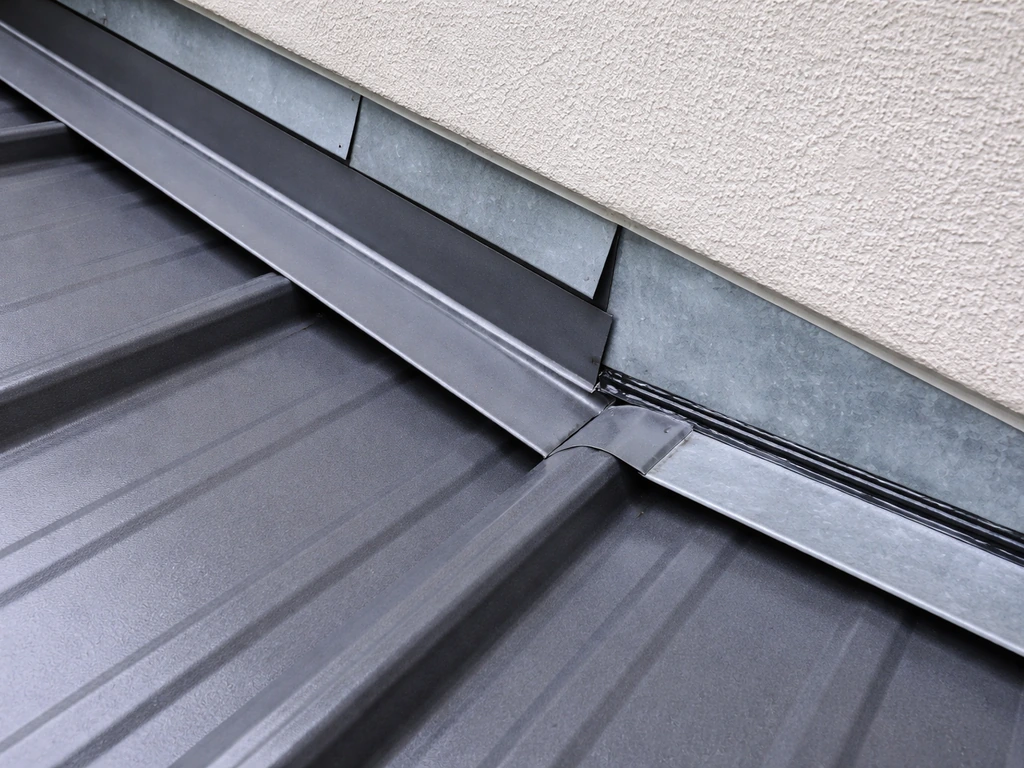 Close-up of roof flashing and sealant at a house wall connection with visible lap lines.