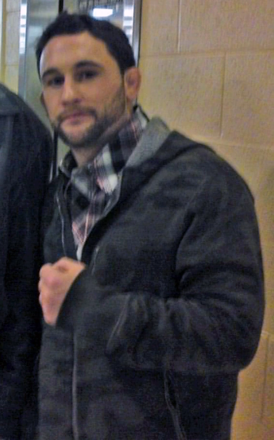 Frankie Edgar posing indoors in a jacket and scarf