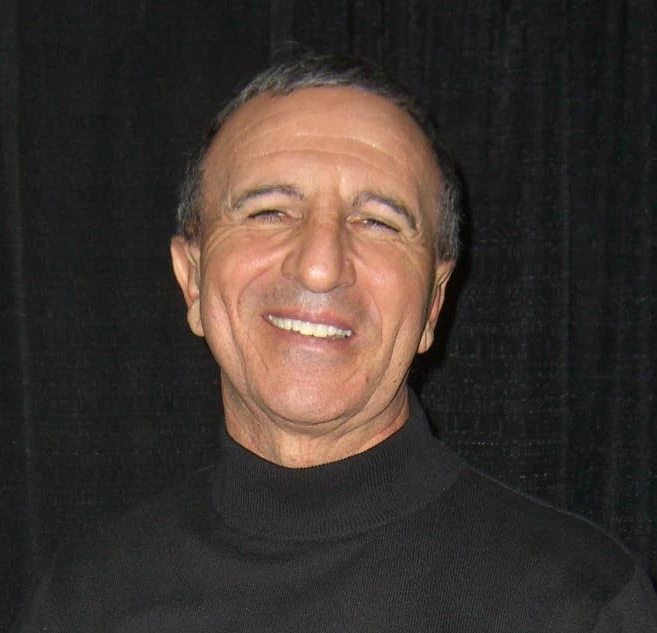 Frank Sivero smiling in a black turtleneck against a dark background