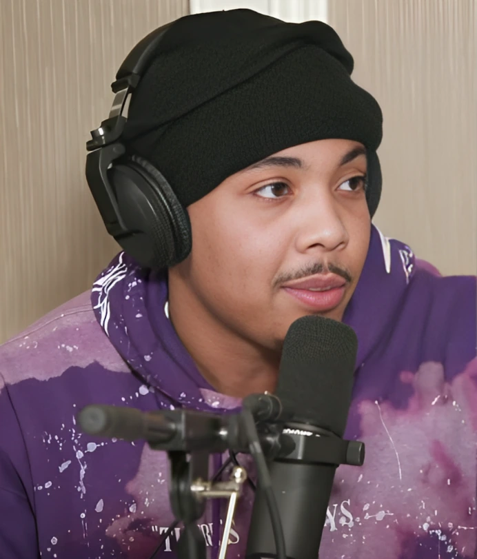 G Herbo speaking into a microphone while wearing headphones and a purple hoodie