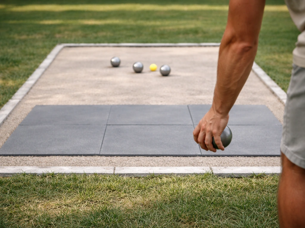Joueur de pétanque tenant une boule près de protections au sol et d’une zone d’impact délimitée sur gazon