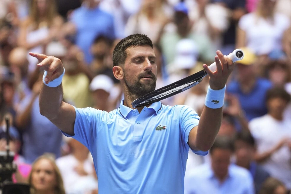 Novak Djokovic sur le court en tenue de tennis, concentré pendant un match avec le public en arrière-plan.