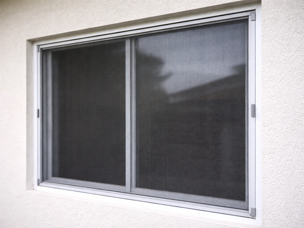 Taut window screen mounted in front of glass, with secure fasteners along the frame edges.