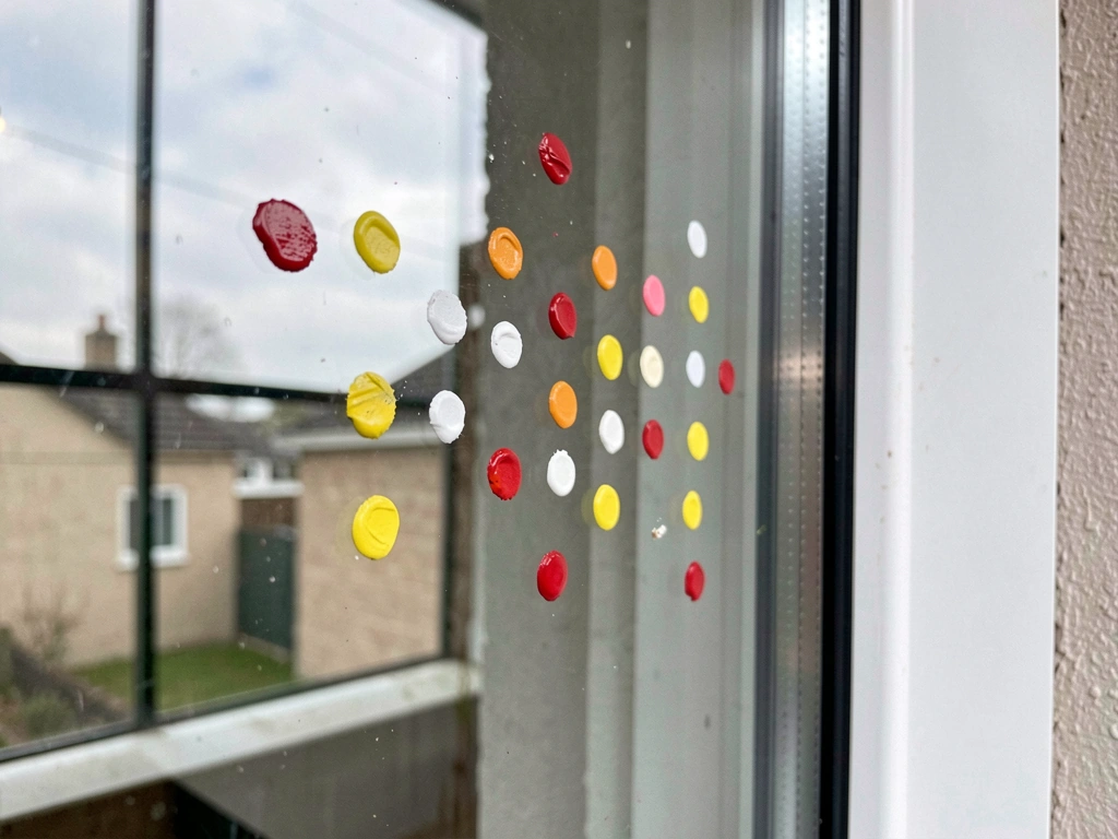 Hand placing exterior bird-window dots on a reflective window in a tight spacing grid.