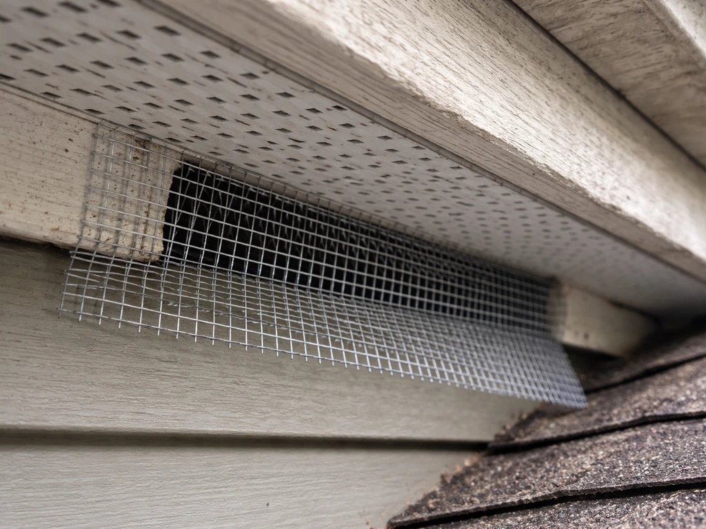 Close-up of a roof soffit gap being sealed with half-inch galvanized hardware cloth.