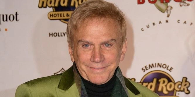 Osmel Sousa at an event, wearing a green jacket and posing in front of a branded backdrop.