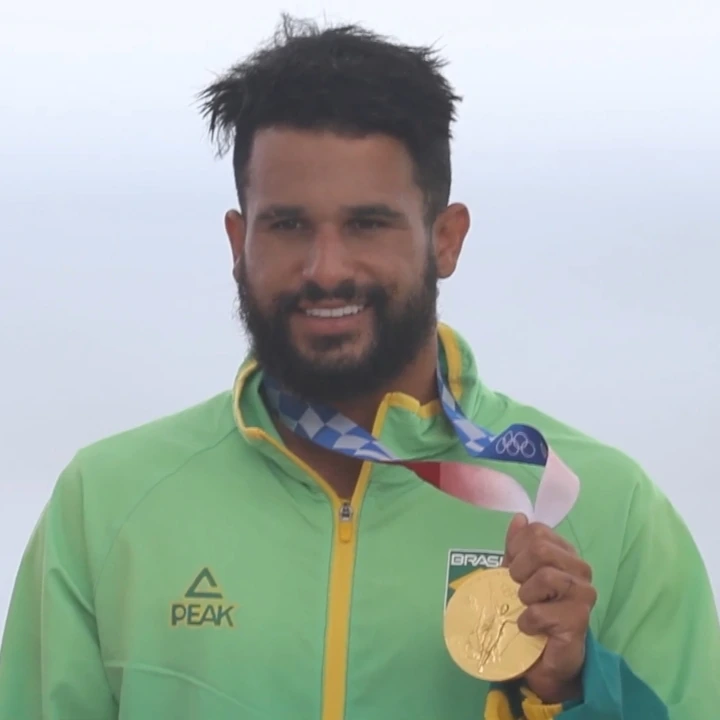 Italo Ferreira smiling in a green Brazil jacket holding up a gold medal
