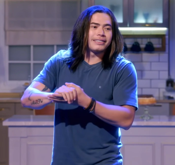 Whindersson Nunes on stage in a blue shirt, speaking during a performance or TV appearance.