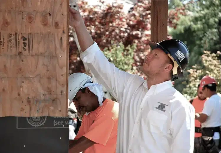 Construction worker in a hard hat inspecting or adjusting wooden framing on a job site