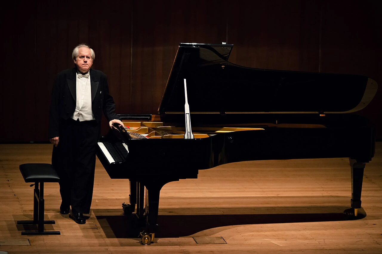 Grigory Sokolov standing beside a grand piano on stage