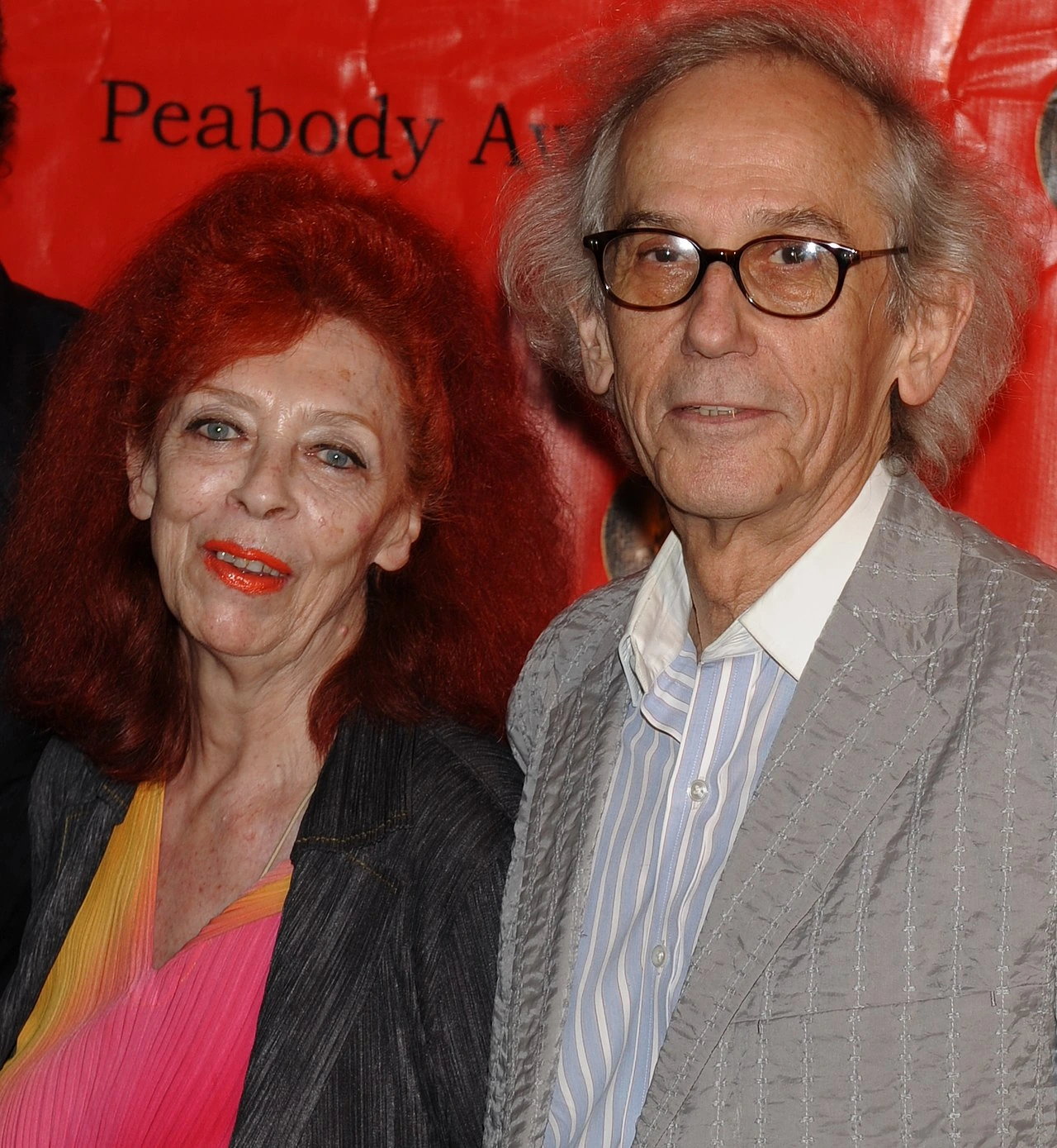 Christo posing with Jeanne-Claude at an event, in front of a red backdrop.