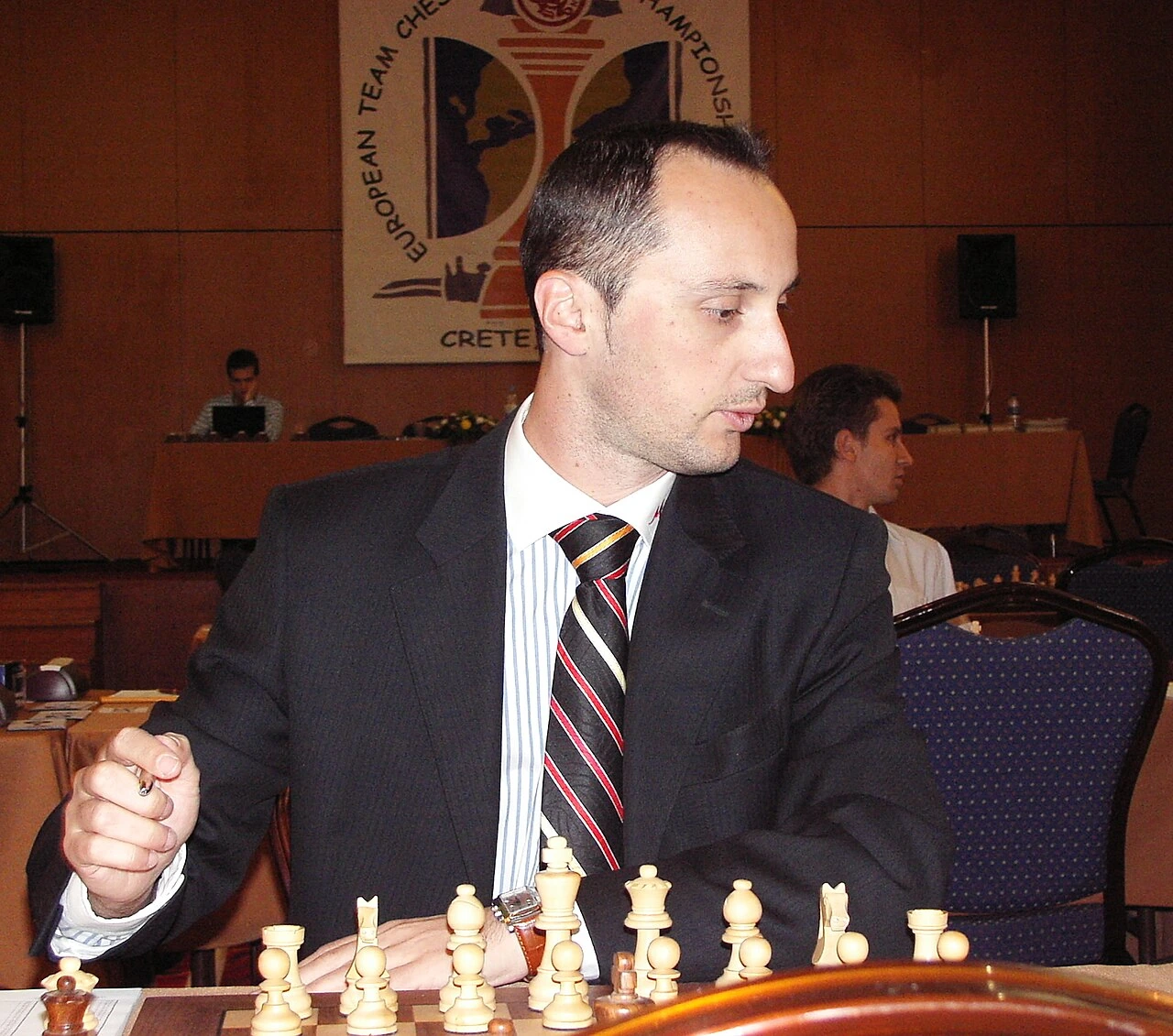 Veselin Topalov seated at a chessboard during a tournament, wearing a suit and concentrating on the game.