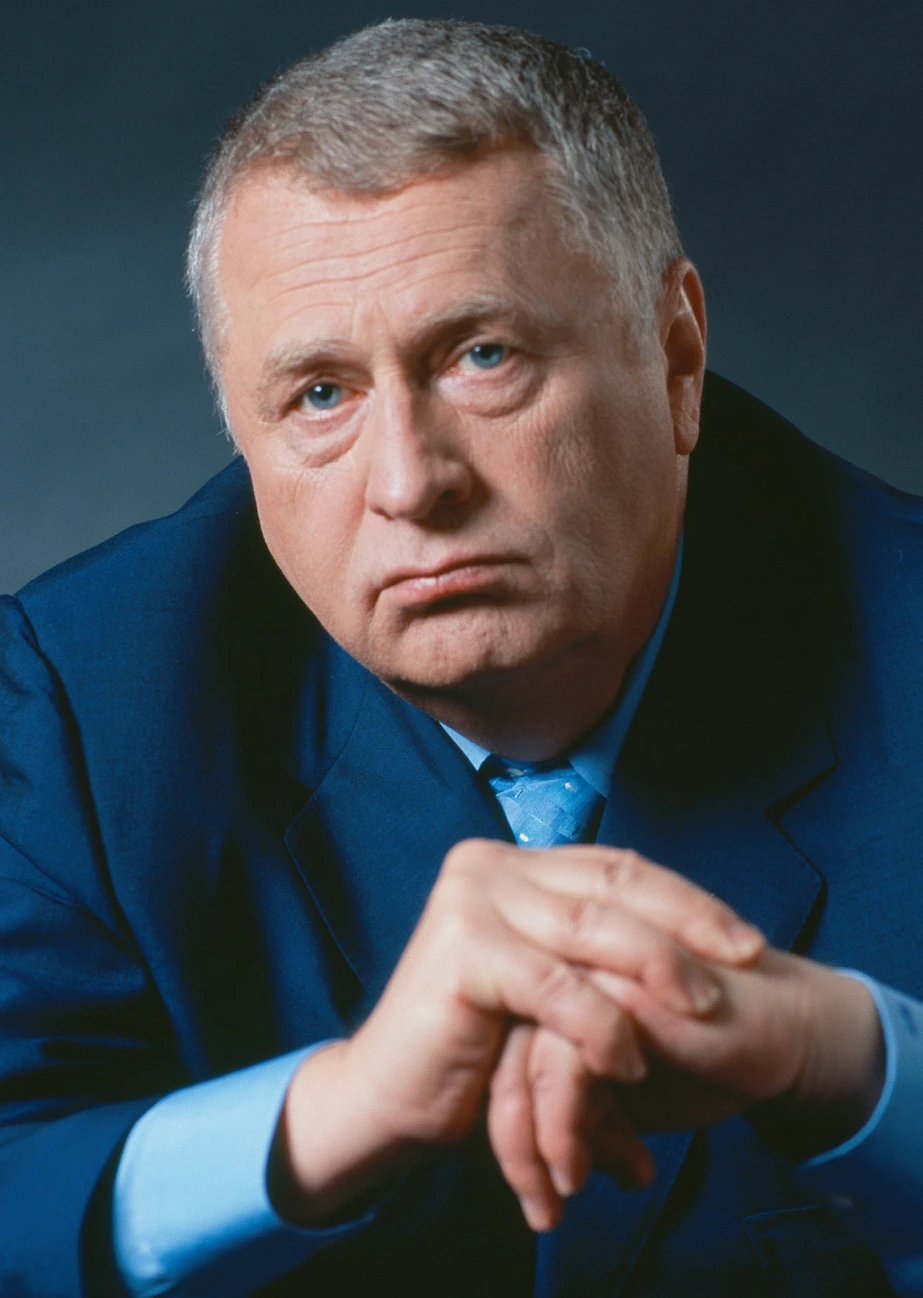 Portrait of Vladimir Zhirinovsky in a blue suit, posed against a dark background.