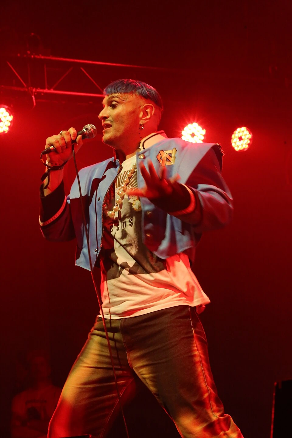 Ivo Dimchev performing on stage under red lights, holding a microphone.