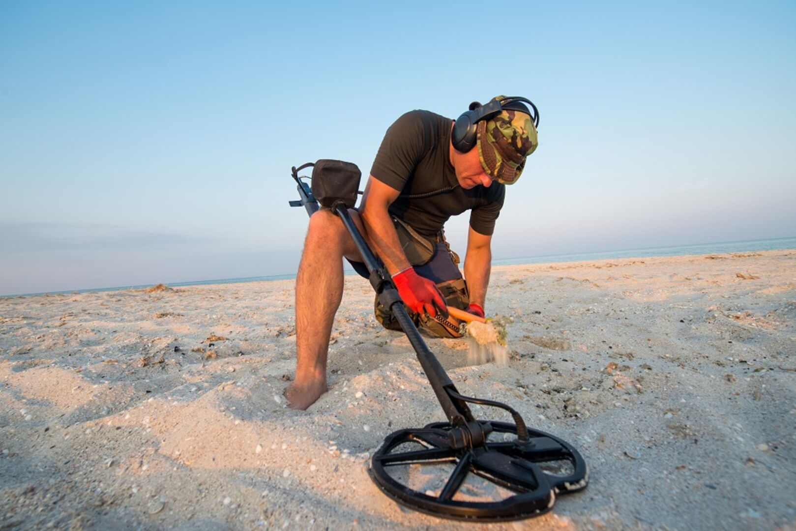 Ein Mann sucht mit einem technischen Gerät an einem Strand im Sand