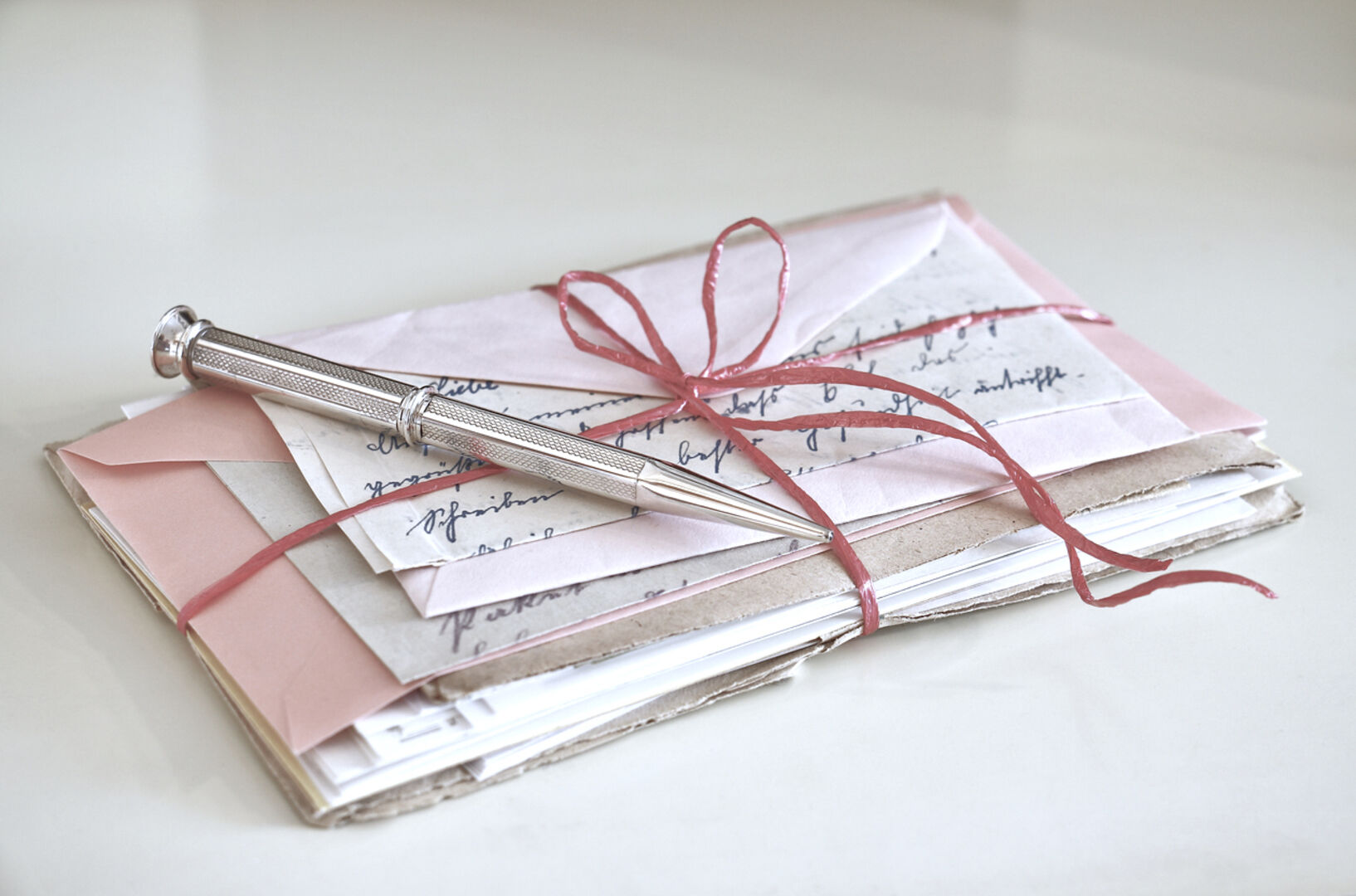 Ein Päckchen Liebesbriefe mit einer roten Schleife verschnürt, darauf ein Kugelschreiber