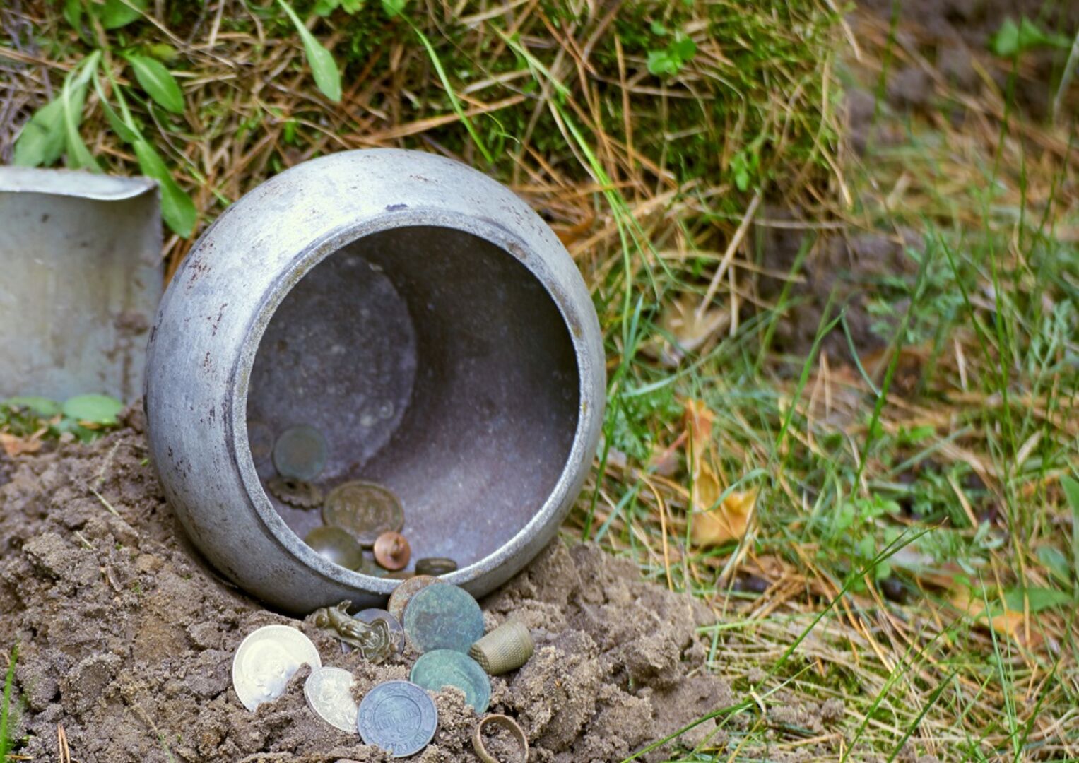 Ein Tongefäß, einzelne Münzen auf Erde