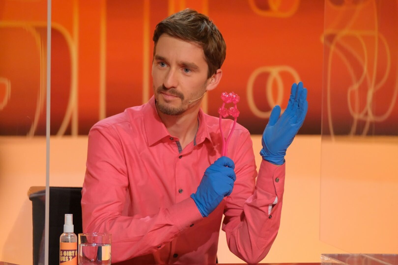 Clemens Maria Schreiner in einem rosa Hemd und blauen Handschuhen in der Sendung &quot;Was gibt es Neues?&quot;