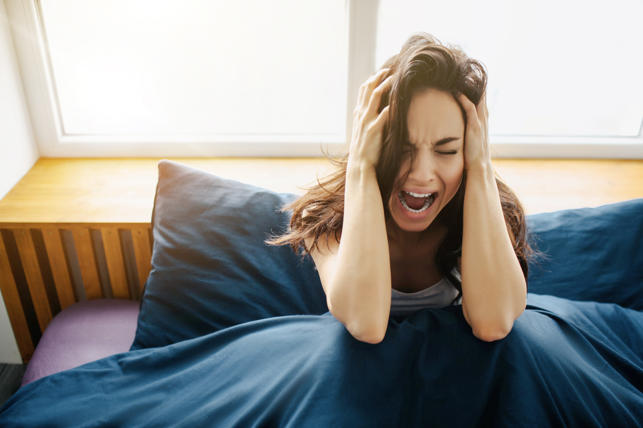 Junge Frau im Bett,  rauft sich die Haare und schreit